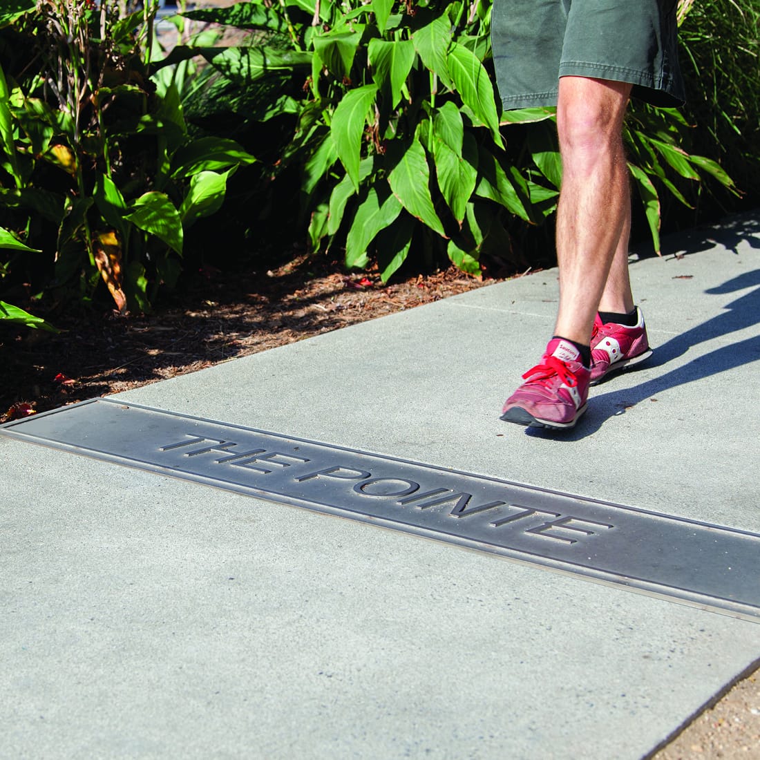 Metal ground plaque reading "THE POINTE," designed by RSM Design, embedded in a sidewalk with a pedestrian walking past in Playa Vista.