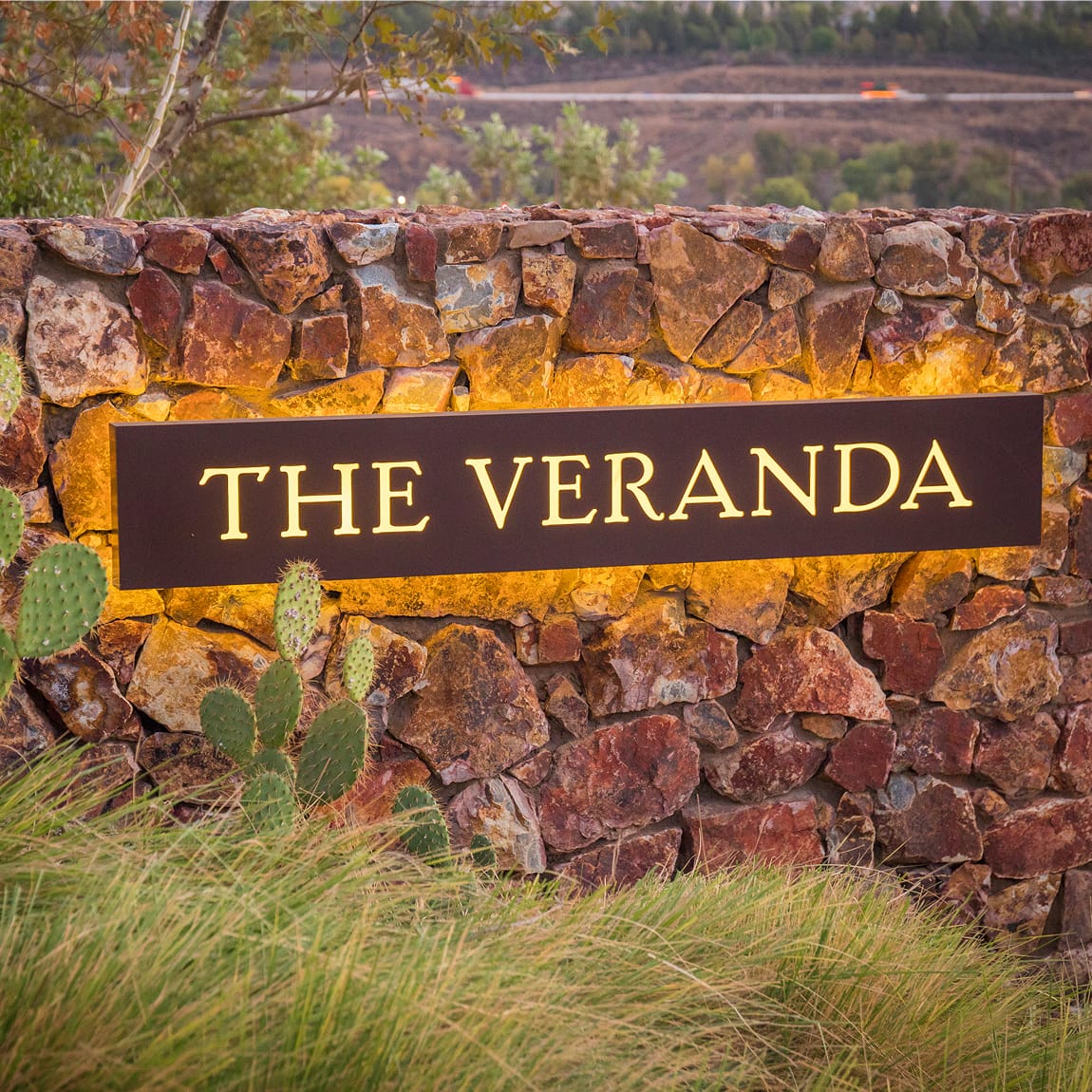Illuminated "The Veranda" sign set into a stone wall with cactus and grasses at Terramor - environmental graphic design by RSM Design