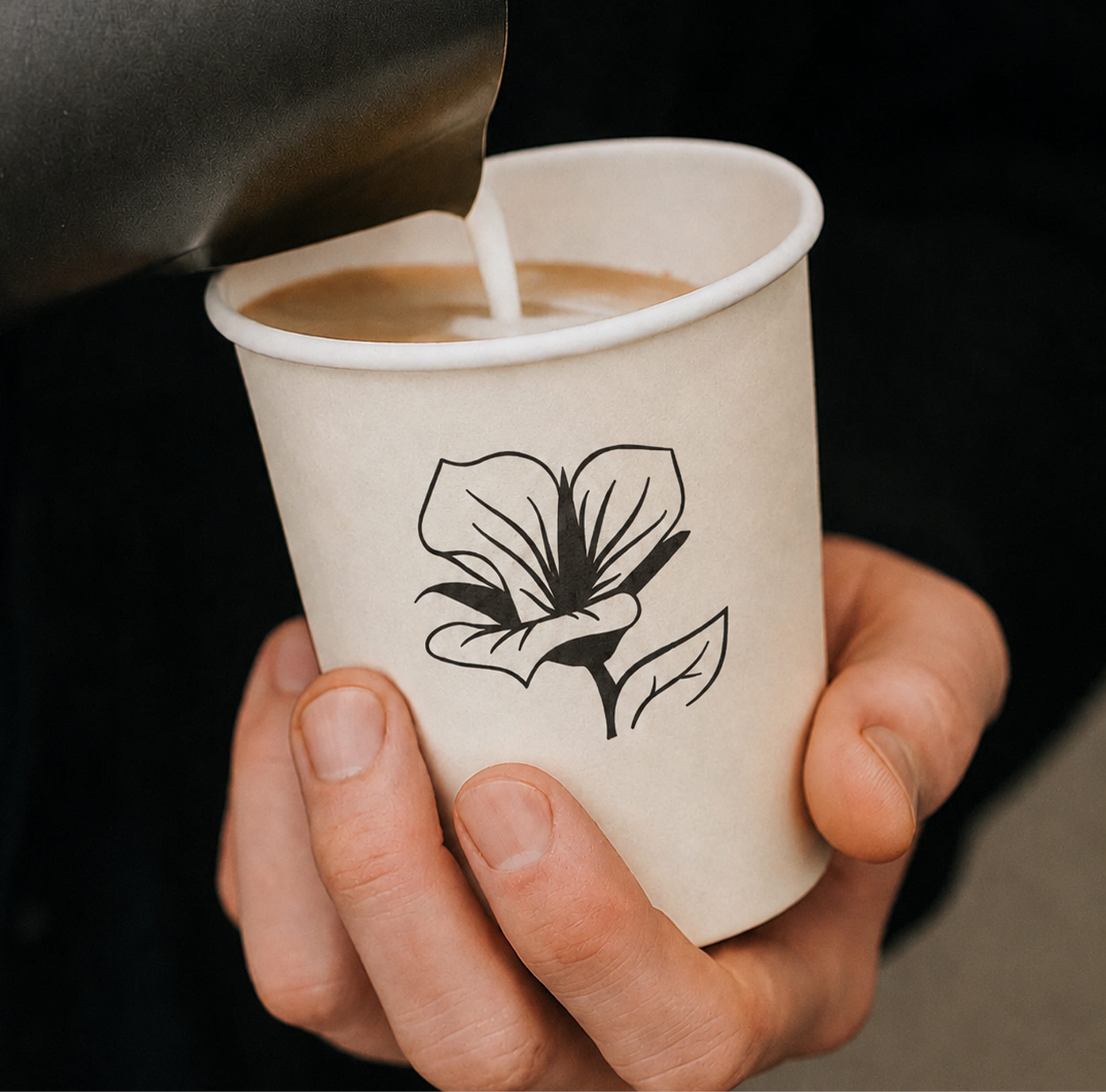 Coffee being poured into a paper cup featuring a hand-drawn magnolia flower logo, held at Mountain View Village in Riverton, Utah — branding and environmental graphic design by RSM Design.
