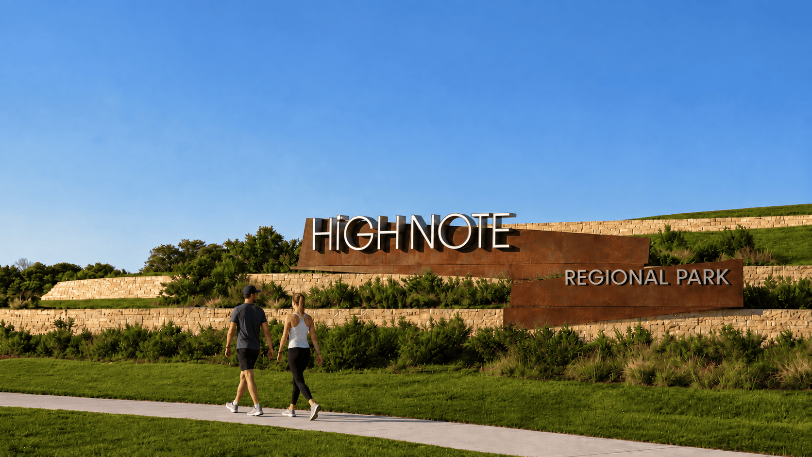 Weathered steel monument sign with dimensional letters reading "HighNote Regional Park" set against a stacked limestone retaining wall, with two pedestrians walking a path in the foreground — environmental graphic design and signage by RSM Design.