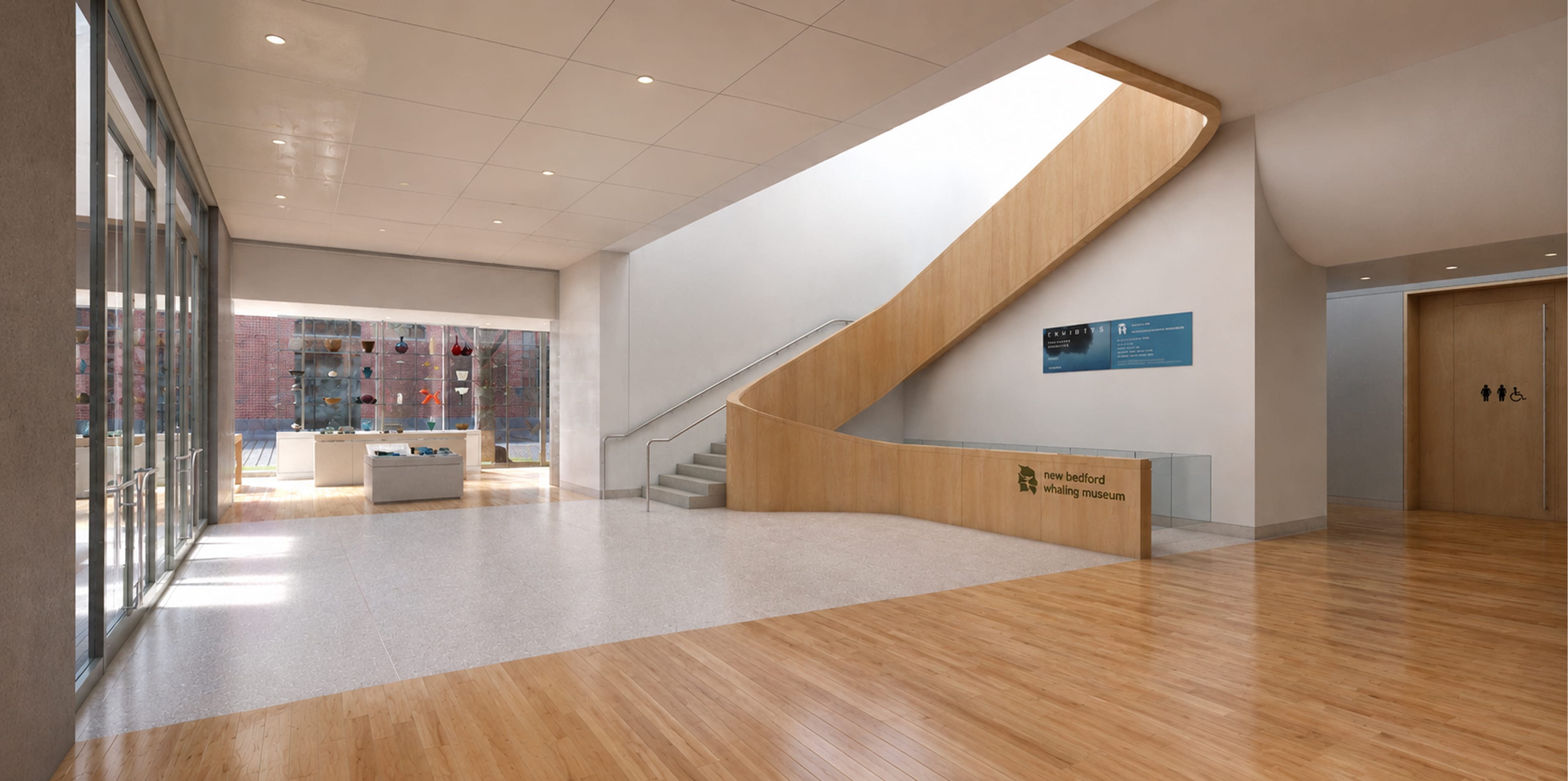 Wood-clad curved staircase wall with logo and lowercase lettering reading "new bedford whaling museum," interior lobby wayfinding and identification signage by RSM Design